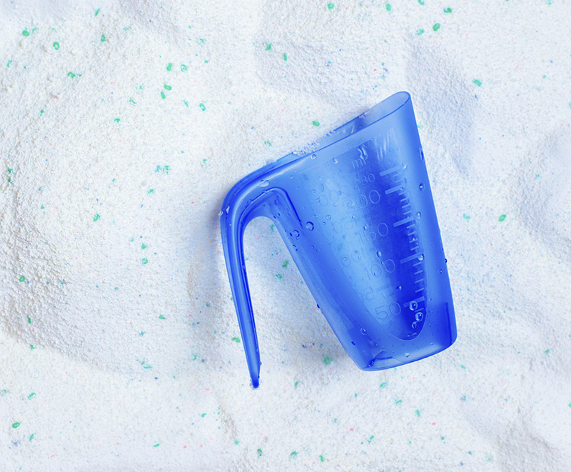 Washing laundry detergent powder and blue plastic measuring cup, top view
