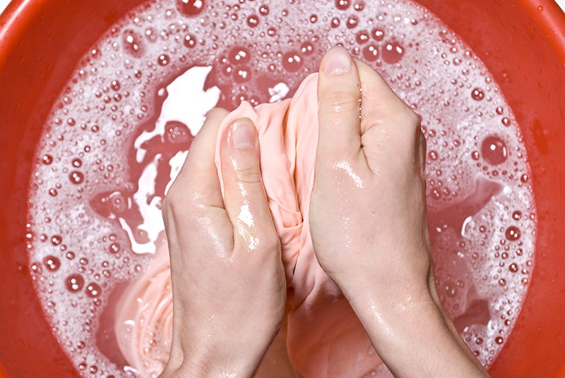 hands washing shirt in a red plastic tub