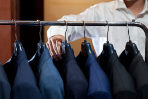 many suits hanging on rack with a man hand