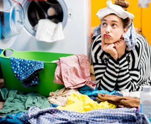 Unhappy housewife sitting with socks near the washing machine with colorful clothes on the floor at home