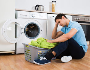 Tensed young man looking at laundry basket at home